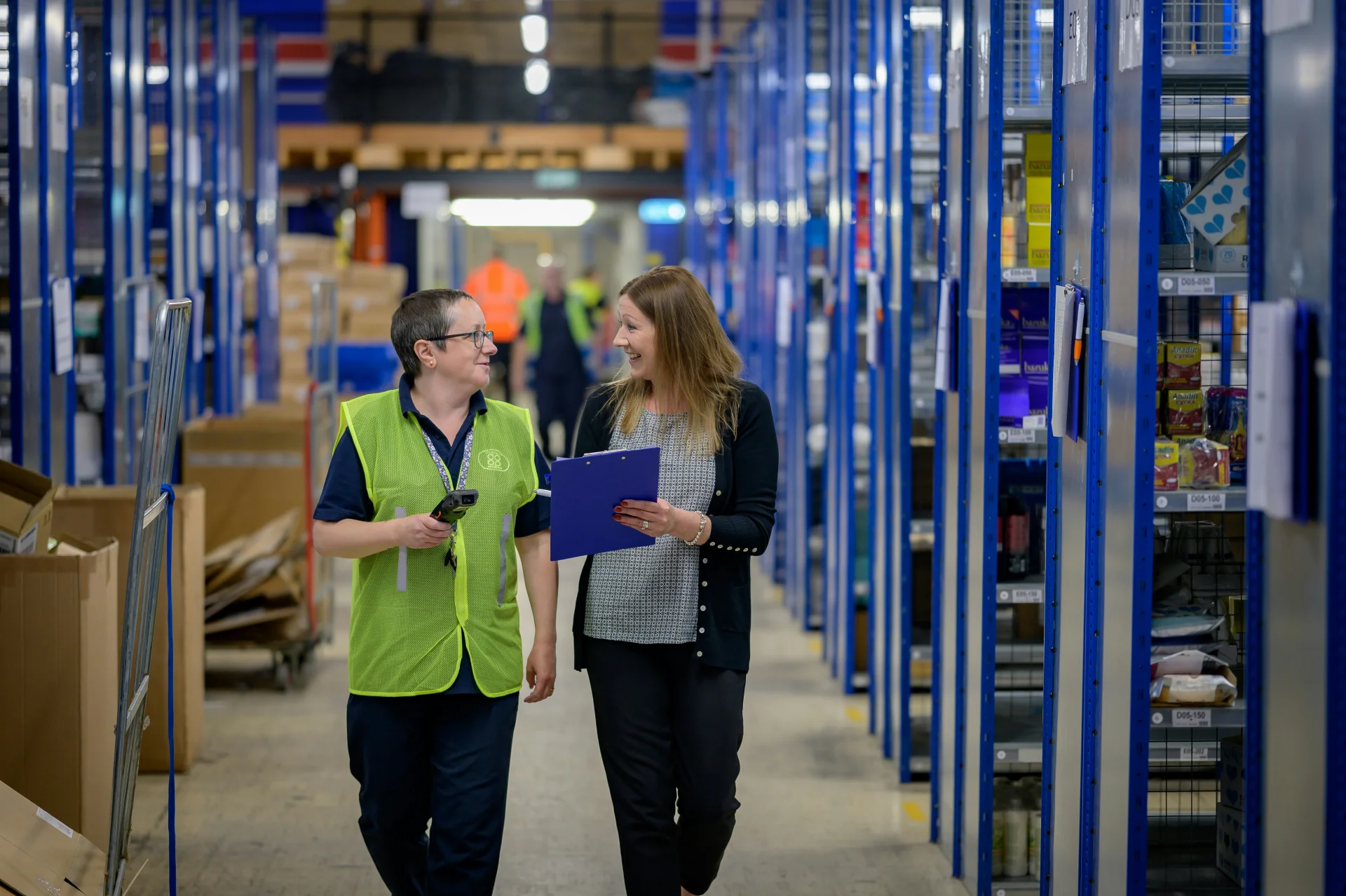 een foto van twee personen in een industriële omgeving die wandelen met een clipboard