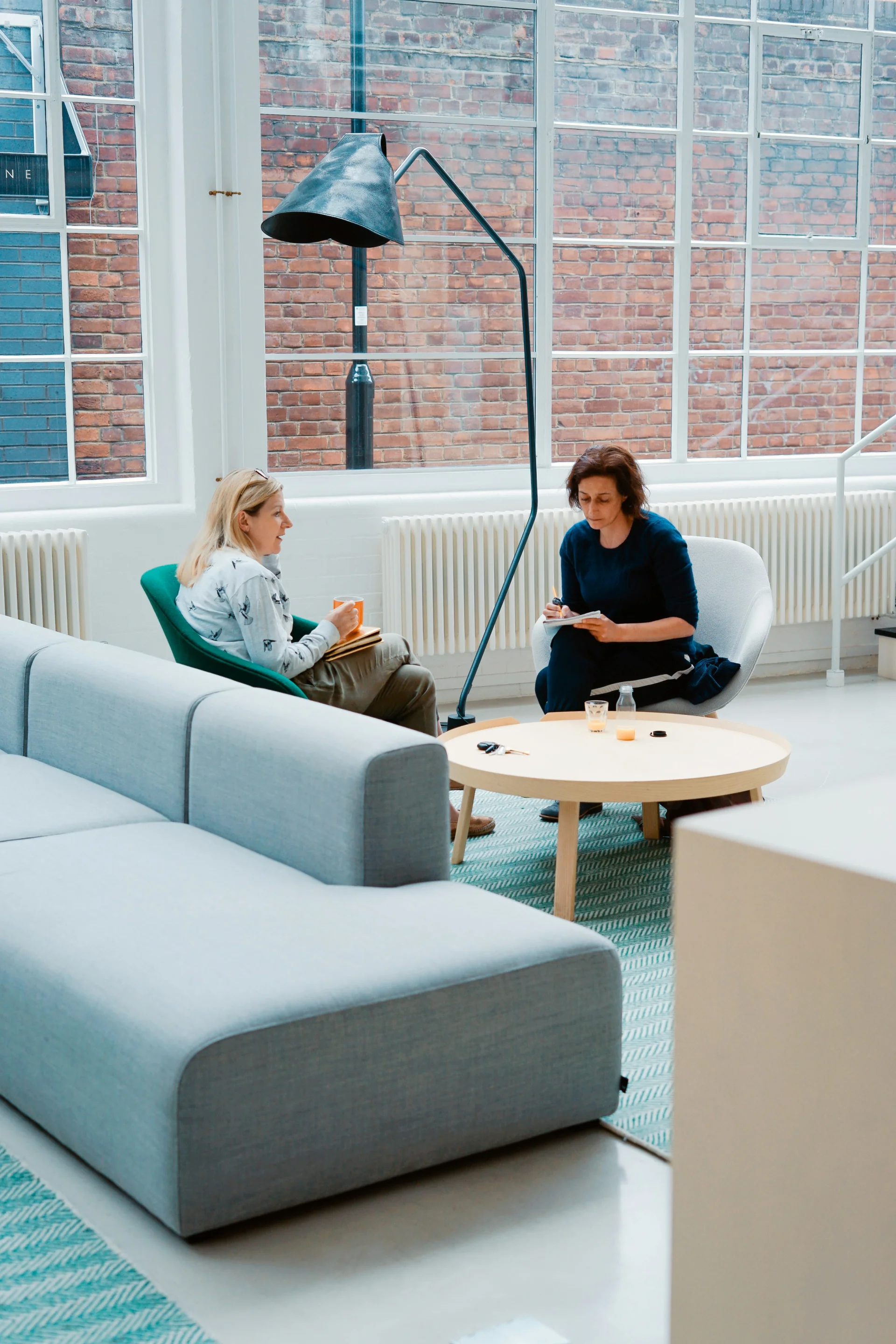 een foto van twee personen in een salon die aan het praten zijn, één persoon neemt notities