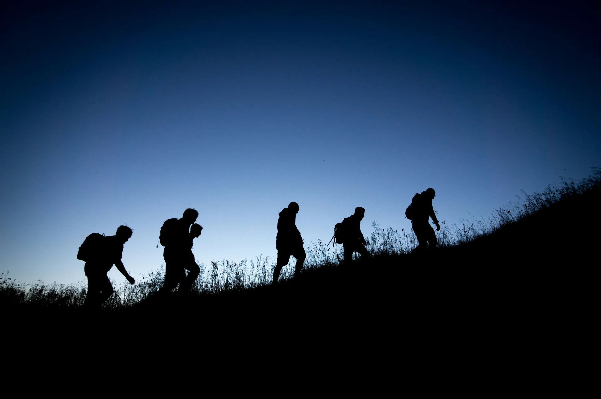 vijf personen die in de nacht over een glooiend veld wandelen