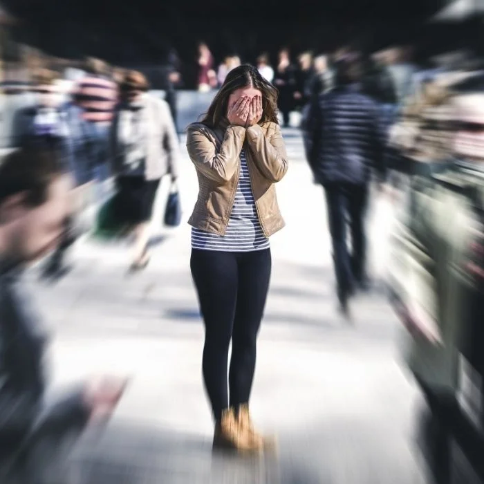 een jonge vrouw in het midden van een mensenmassa met de handen voor haar gezicht