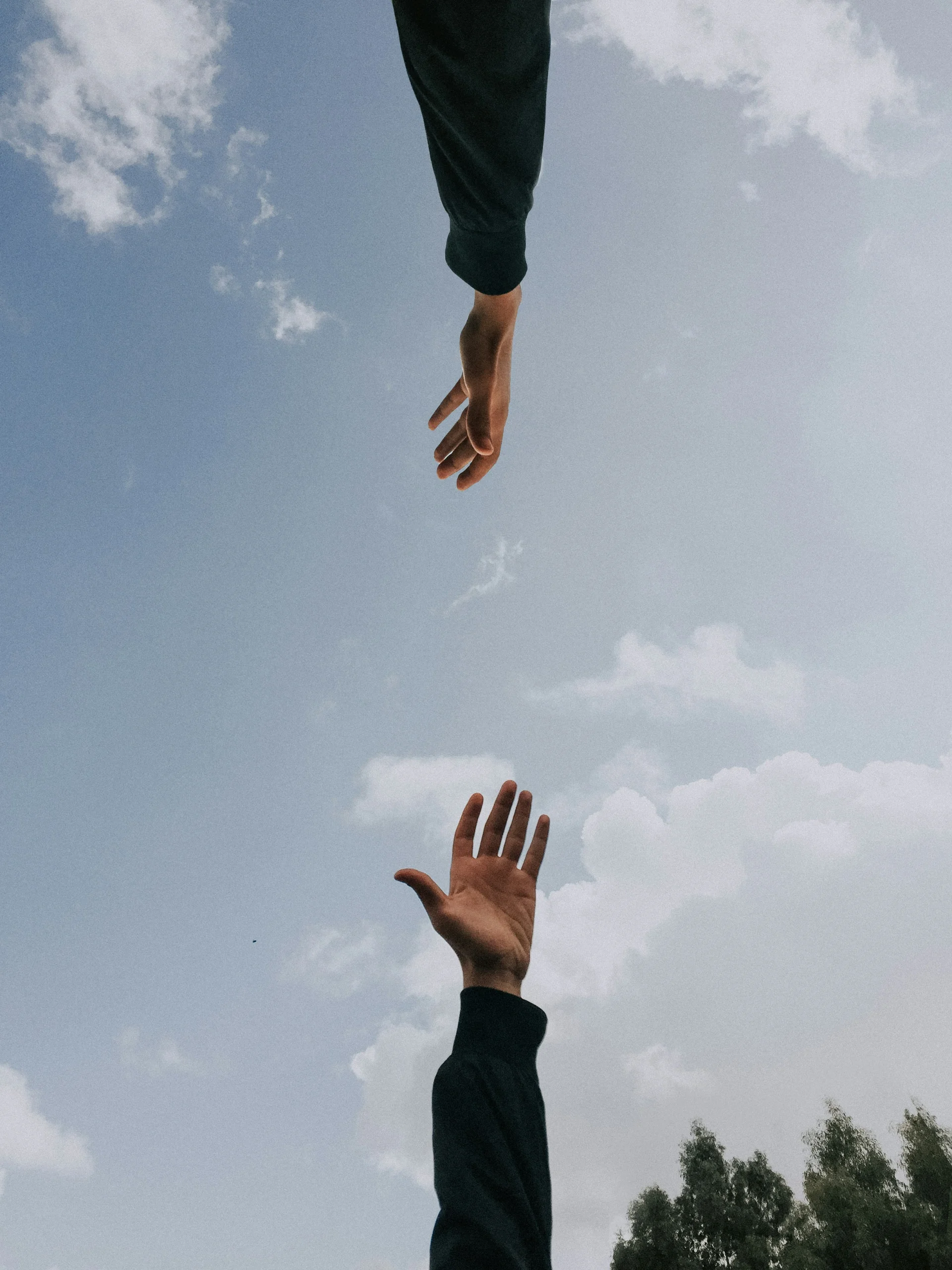 twee handen die naar elkaar reiken in de lucht 
